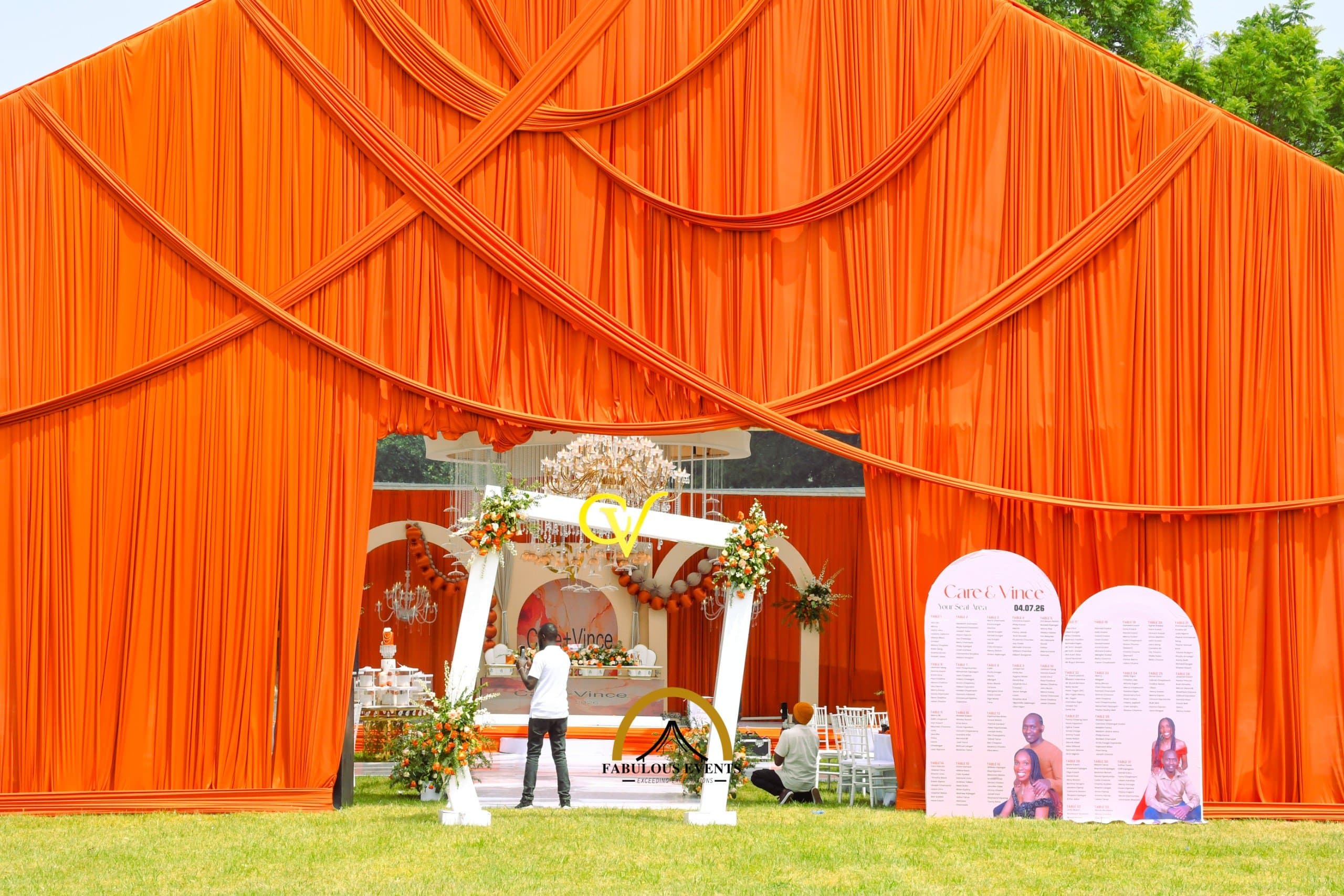 Bold orange draping, elegant florals, and a stunning chandelier creating a truly unforgettable wedding entrance.
